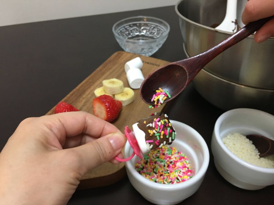 カラースプレーをチョコレートがかかったマシュマロにトッピング