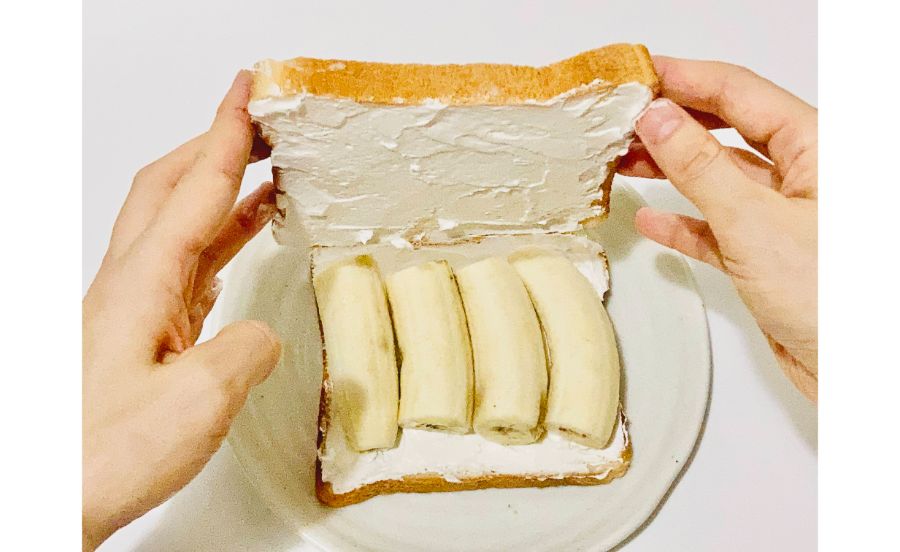 生クリームをぬった食パンの上にバナナを並べたところに食パンを乗せているところ